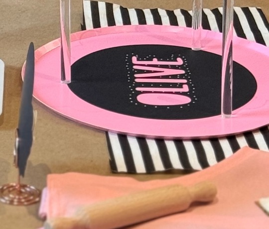 Pink place setting on a black and white striped napkin with a small rolling pin